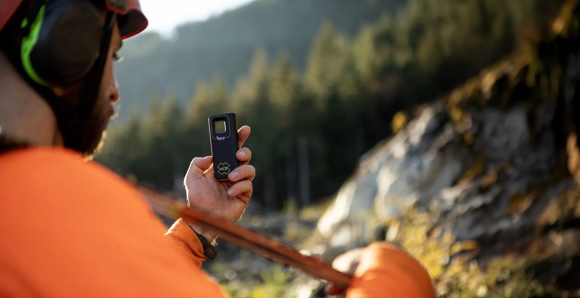 Field worker holding an ACR Bivy Stick satellite communicator in a forested area.