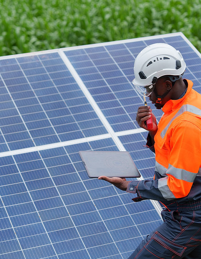Engineer in safety gear inspecting solar panels while holding a tablet.