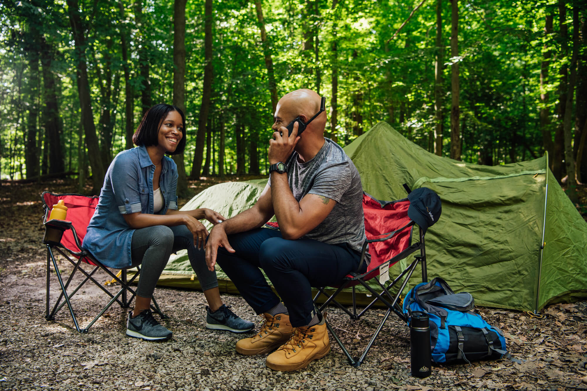 Couple camping in the forest using a satellite phone to stay connected outdoors.