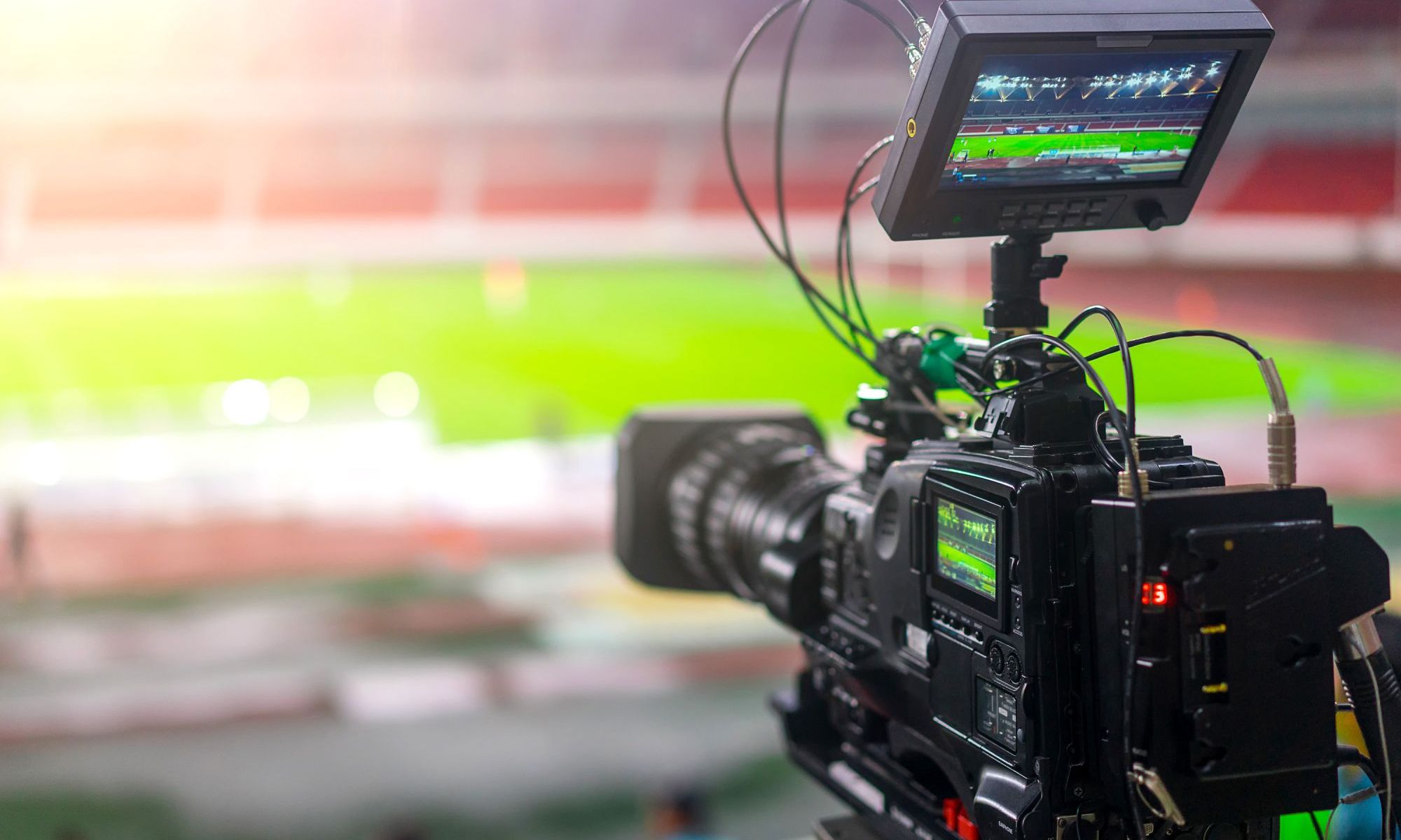 Broadcast camera capturing a live sports event with the field visible on its monitor