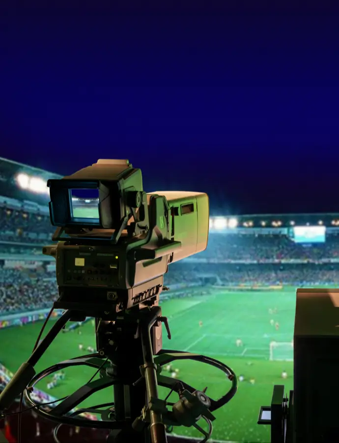 Broadcast camera filming a brightly lit stadium during a live sports match