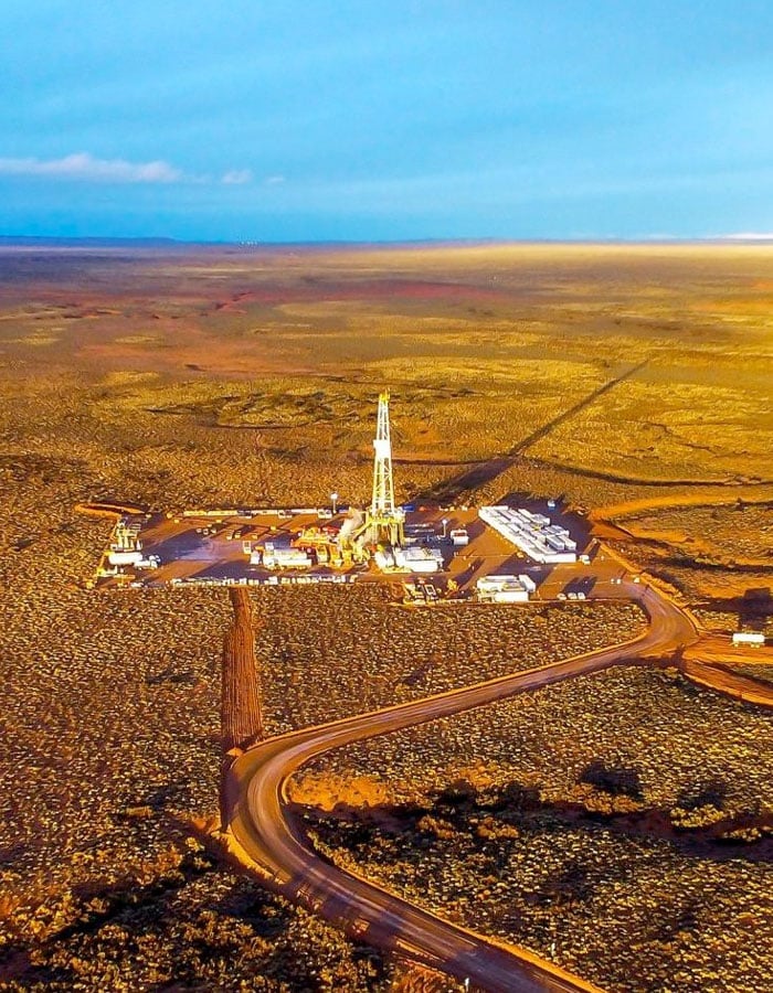 Aerial view of a remote oil drilling site in a vast desert landscape with access roads and equipment