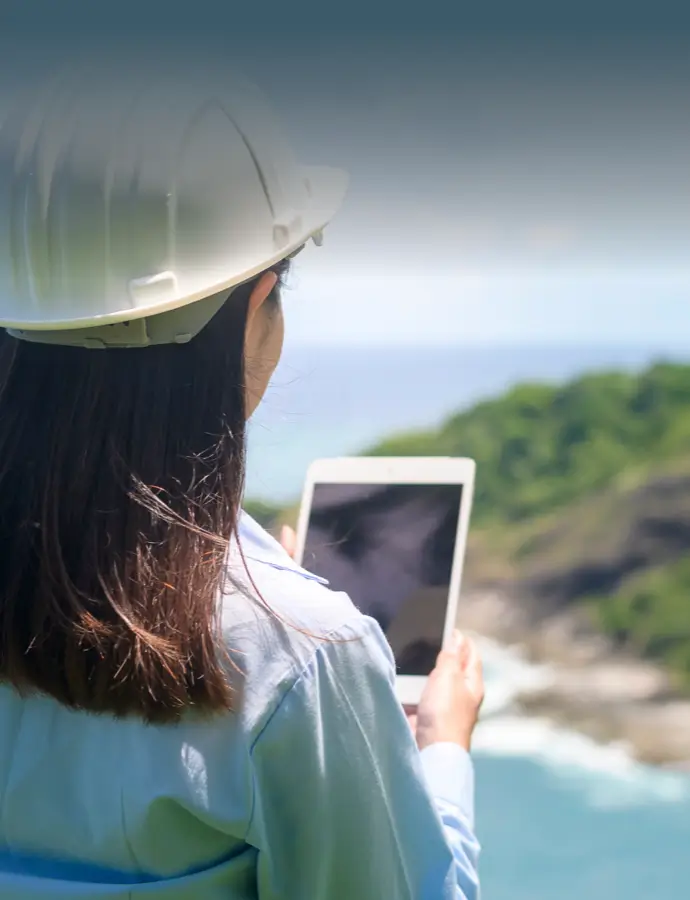 Person in a hard hat using a tablet while overlooking a coastal landscape.